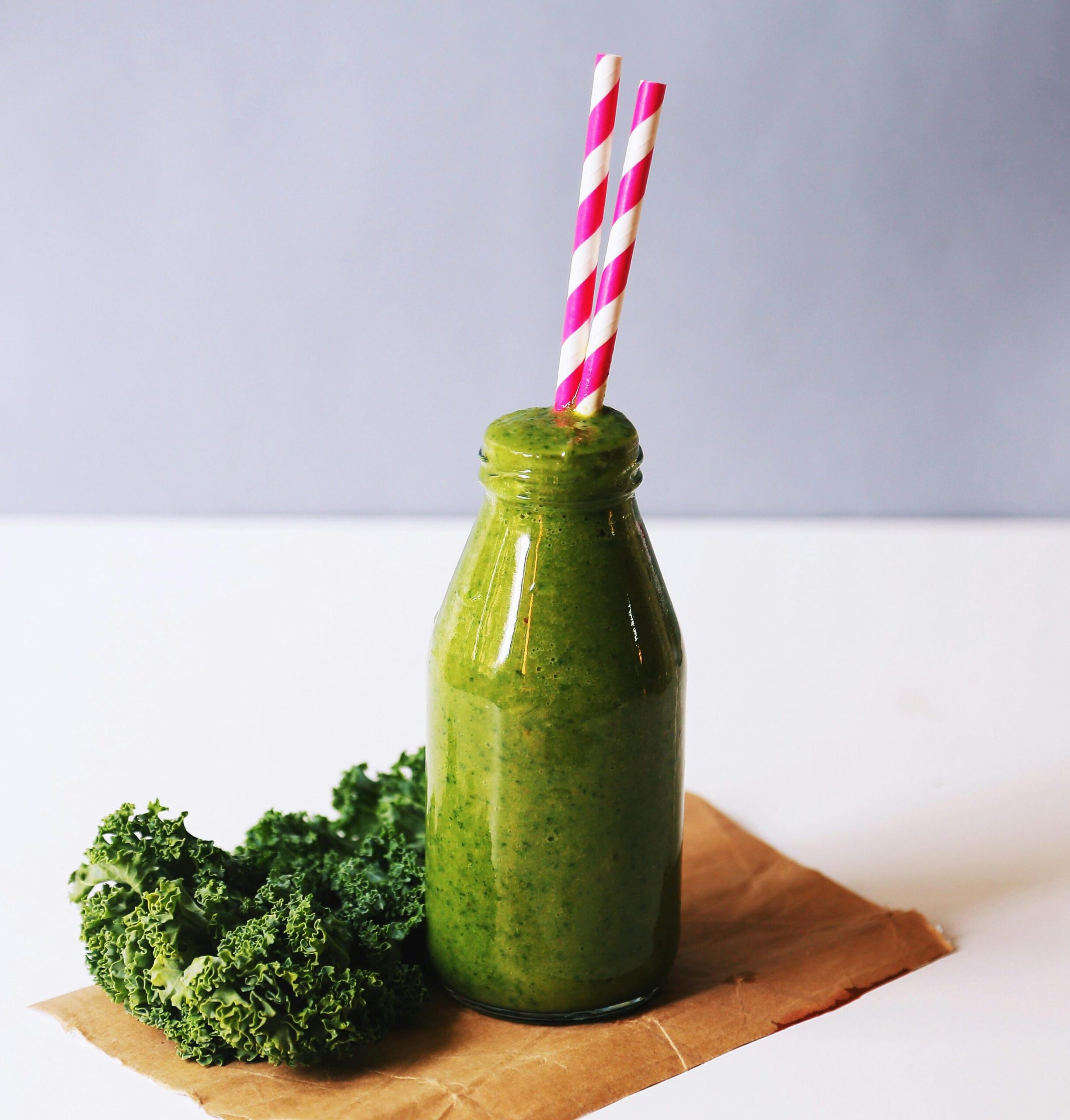 Energizing green smoothie with kale, served in a bottle with vibrant straws for a healthy lifestyle.